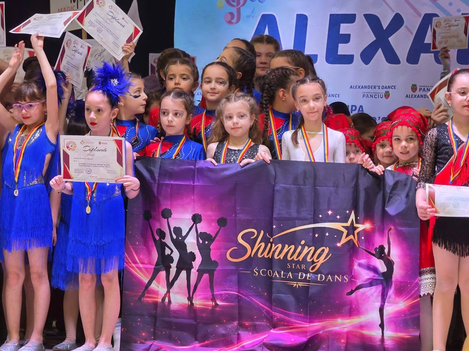 Copiii Shining Star pe podium cu diplome și bannerul oficial al școlii de dans